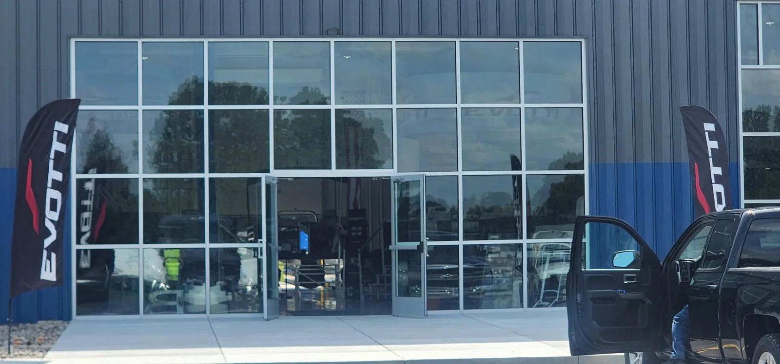 Aluminum-framed glass storefront entrance with open double doors on a blue metal building.