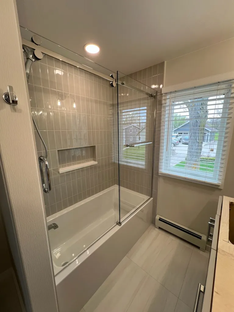 Sliding glass tub enclosure with chrome rollers over a white bathtub in Jackson, MI.